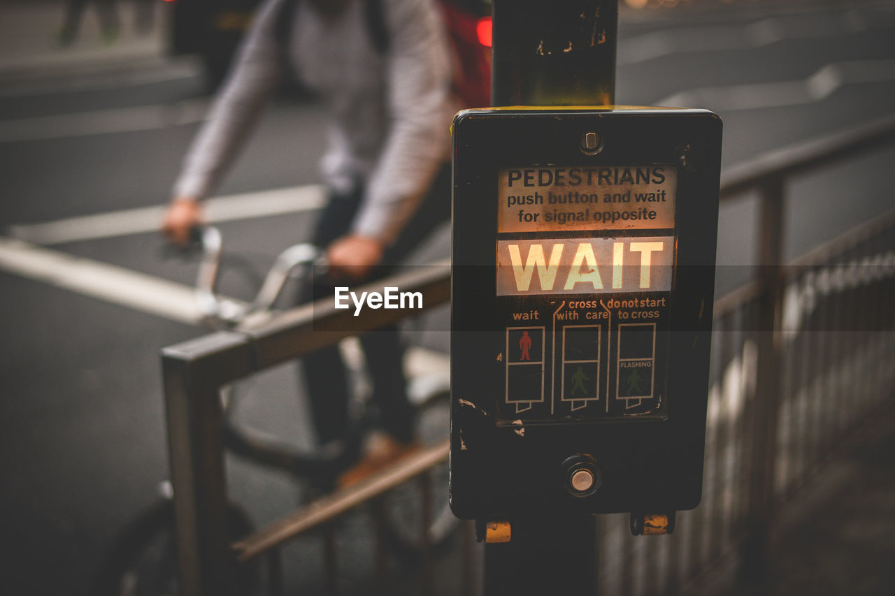 Close-up of road sign against man riding bicycle on city street