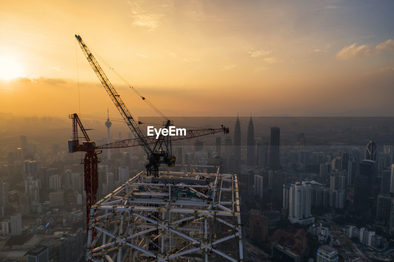 Cranes at construction site in city against sky during sunset