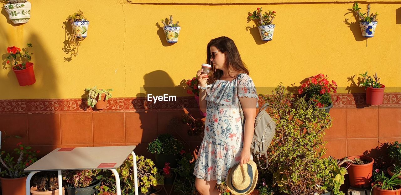 Beautiful woman having coffee while standing against yellow wall
