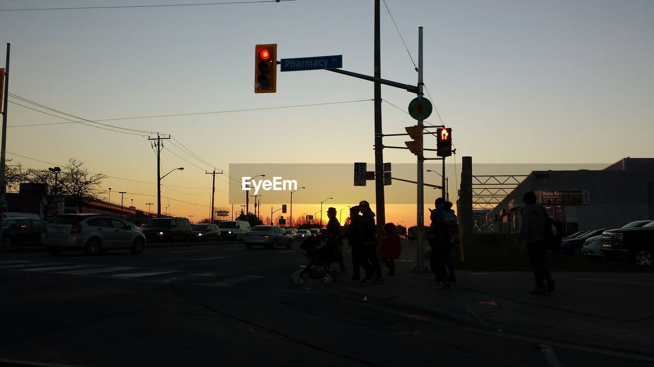 Silhouette people on street by road signal against clear sky during sunset