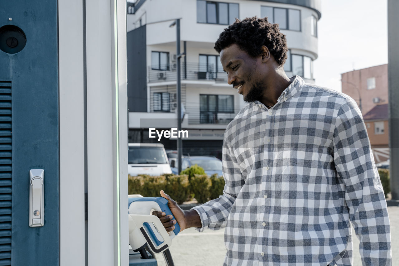 Smiling young man holding car charger at station