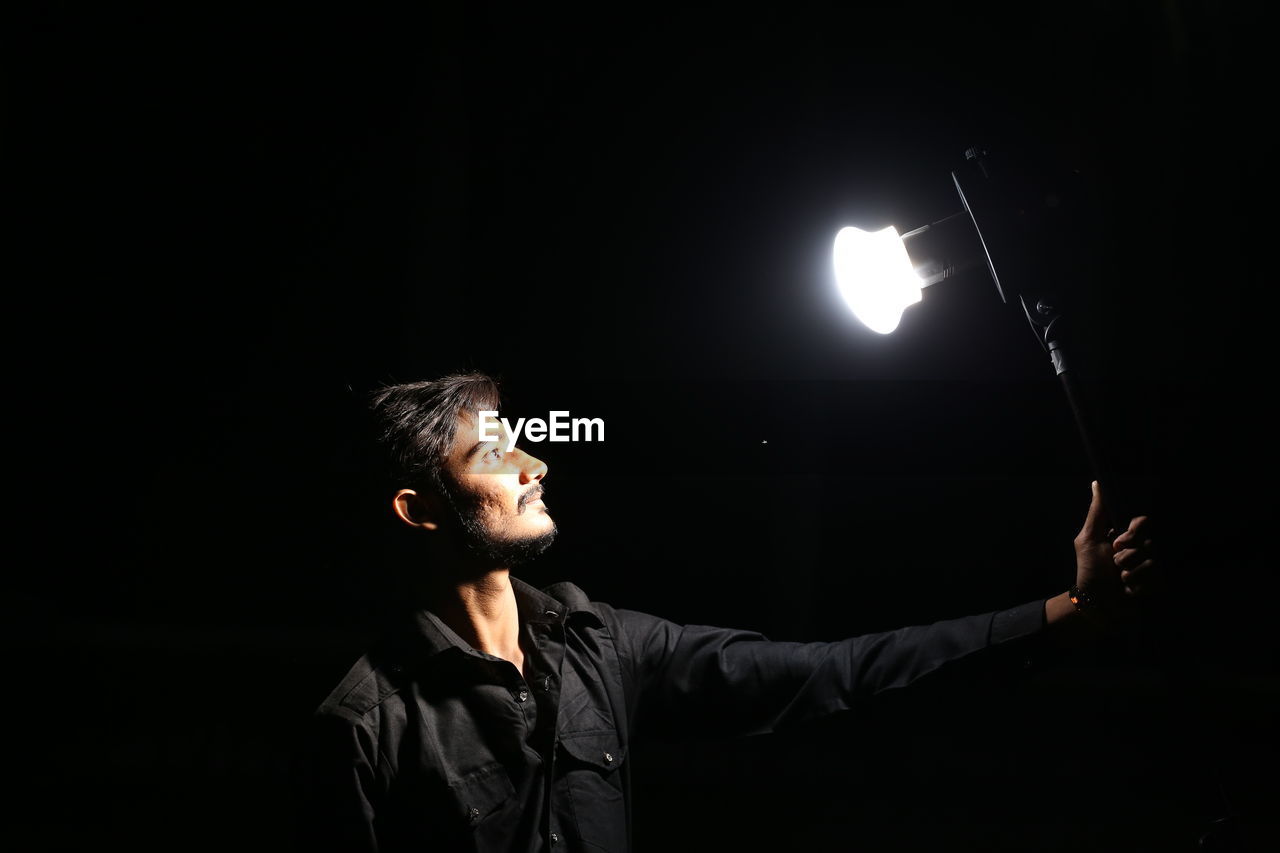 Man looking at illuminated light against black background