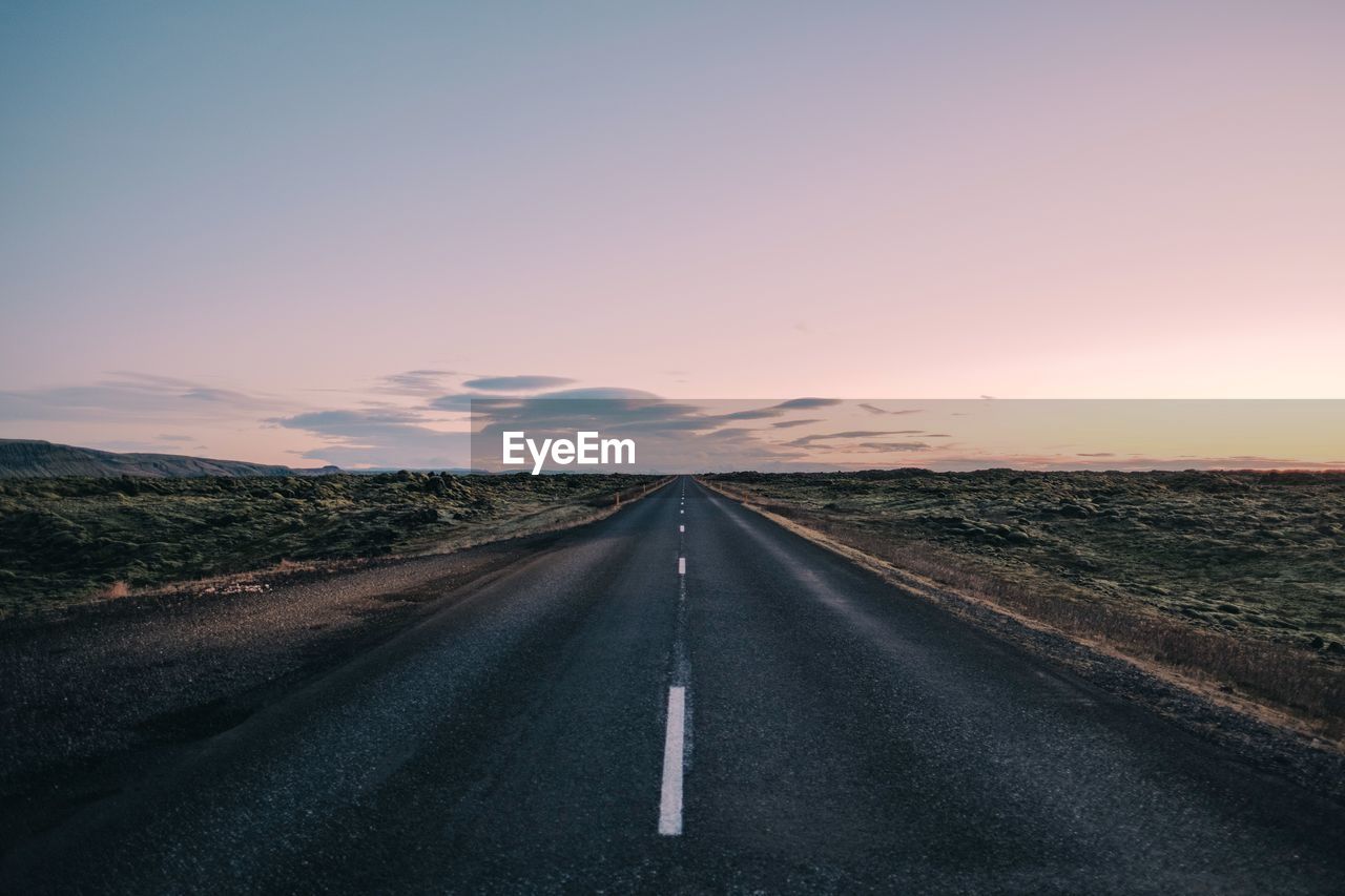 Empty road amidst field against sky during sunset