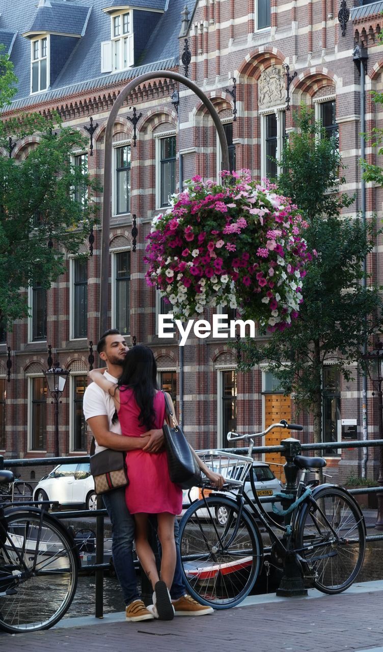 WOMAN CYCLING ON STREET AMIDST BUILDINGS