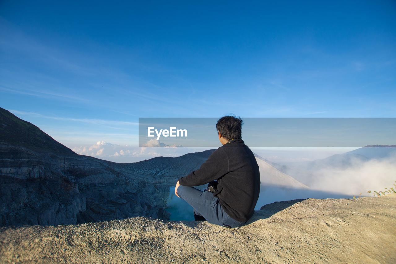 Man looking at view while sitting on mountain against sky