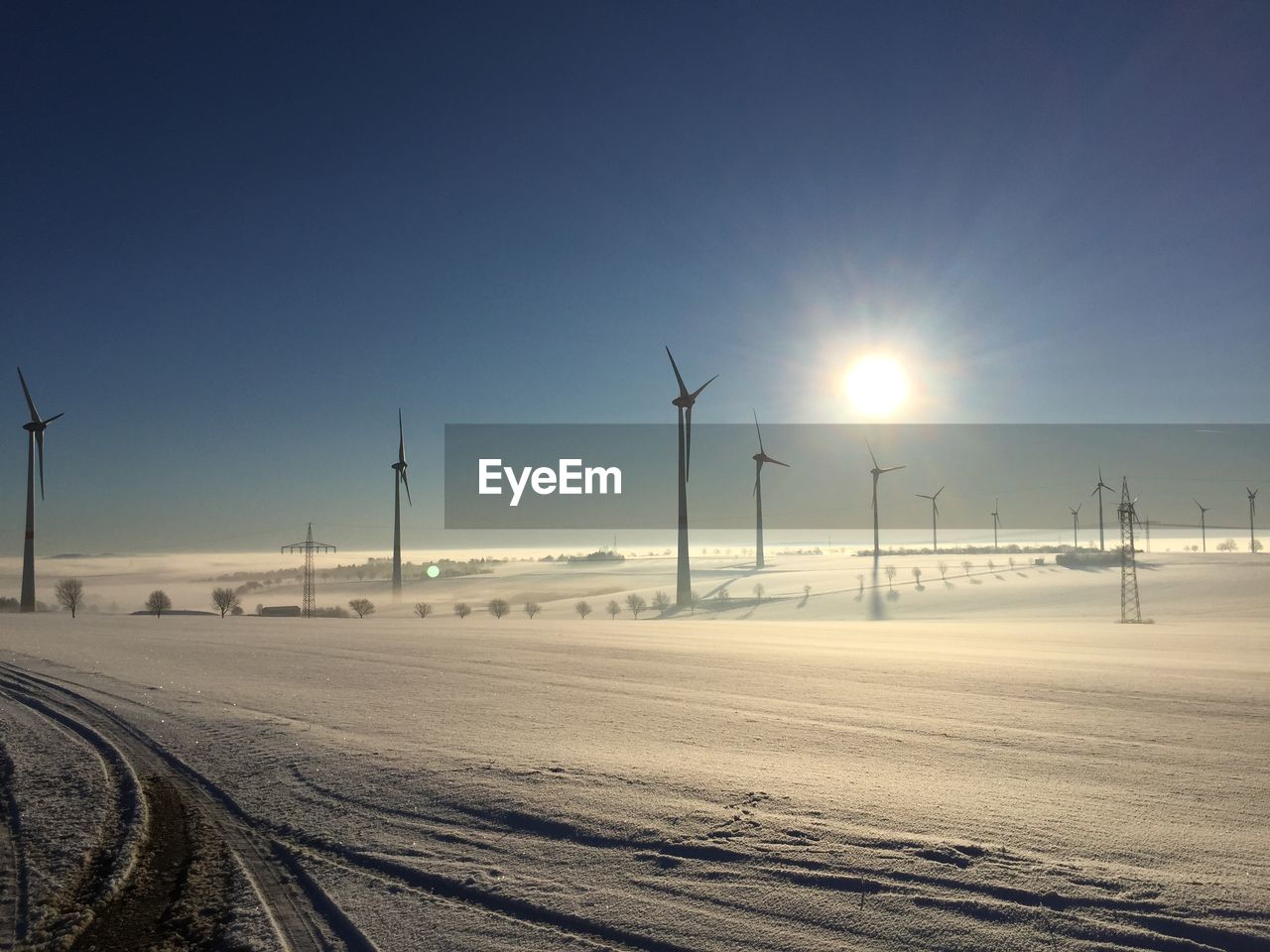 Windmills on snow covered field against sky