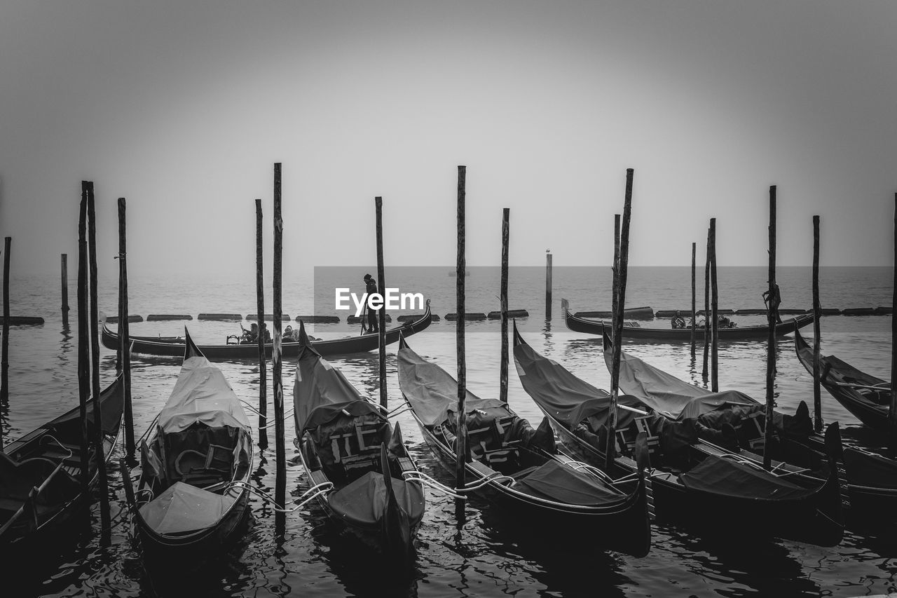 nautical vessel, gondola, water, transportation, black and white, mode of transportation, monochrome, boat, vehicle, wooden post, sea, monochrome photography, nature, moored, travel, travel destinations, sky, post, wood, pole, architecture, lagoon, no people, scenics - nature, canal, tourism, watercraft, outdoors, in a row, tranquility, pier, beauty in nature, clear sky, tranquil scene, mooring post