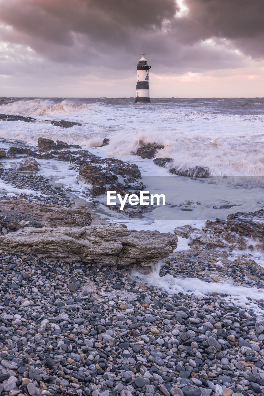 Lighthouse by sea against sky during sunset