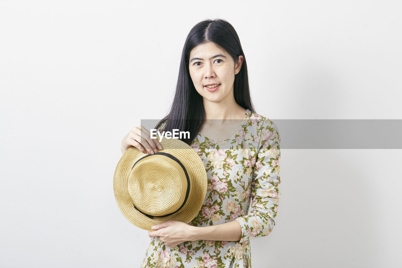 Portrait of smiling woman with hat standing against white background