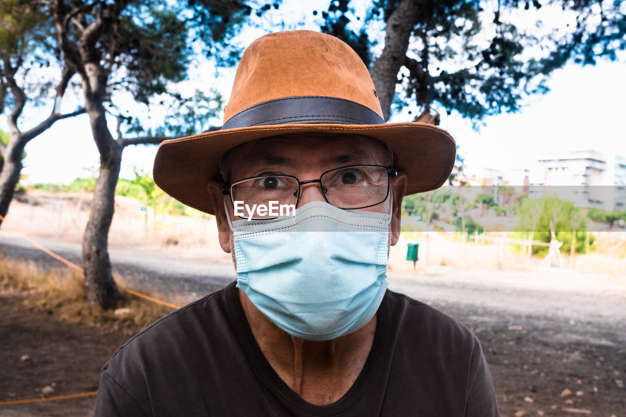 Portrait of man wearing mask and hat against trees