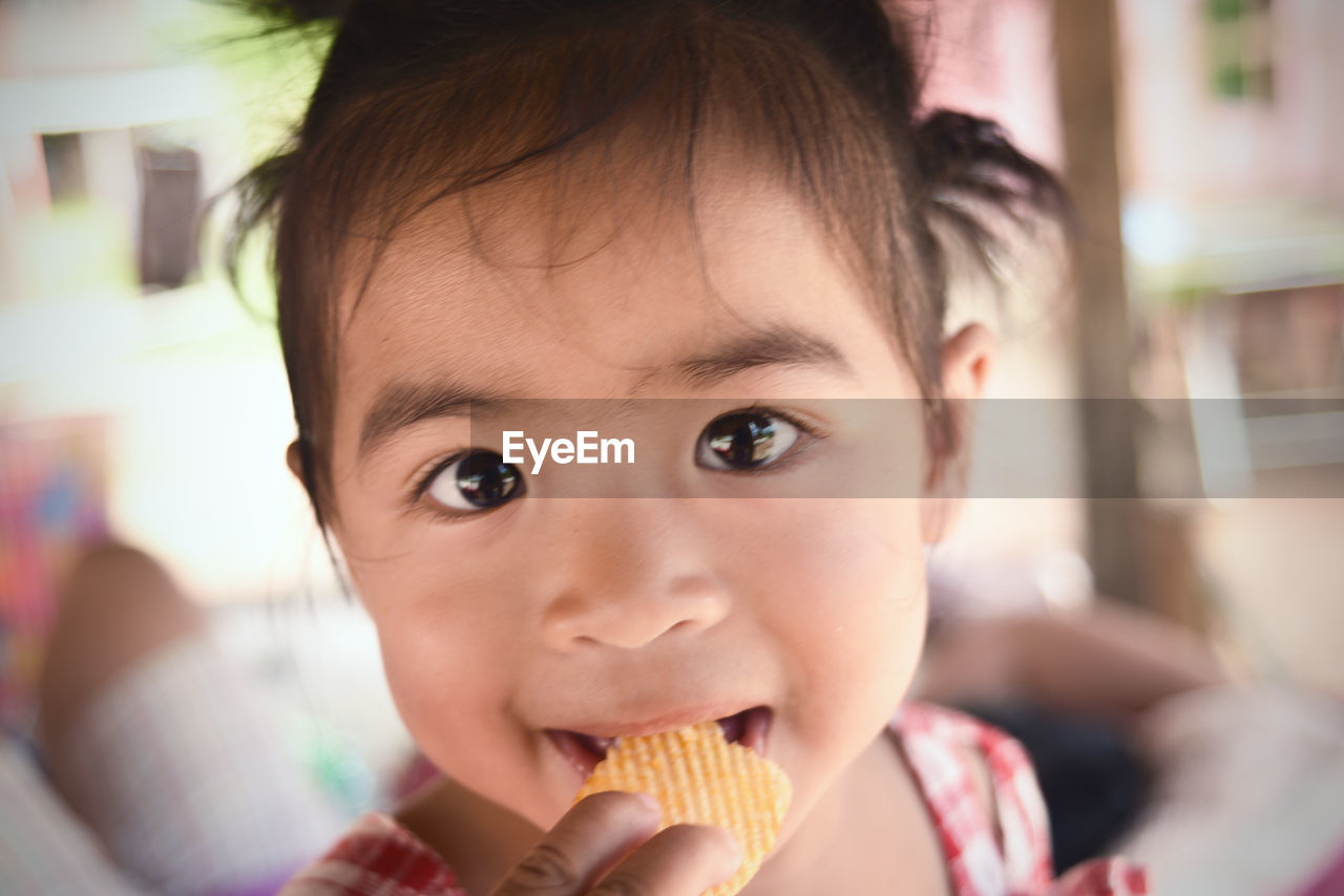 Close-up portrait of cute baby girl eating potato chips