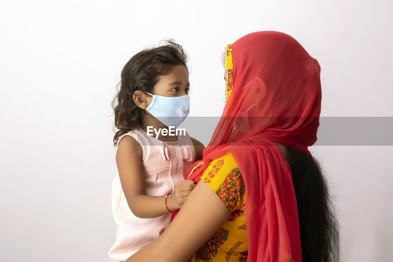 Cute girl wearing flu mask with mother against white background