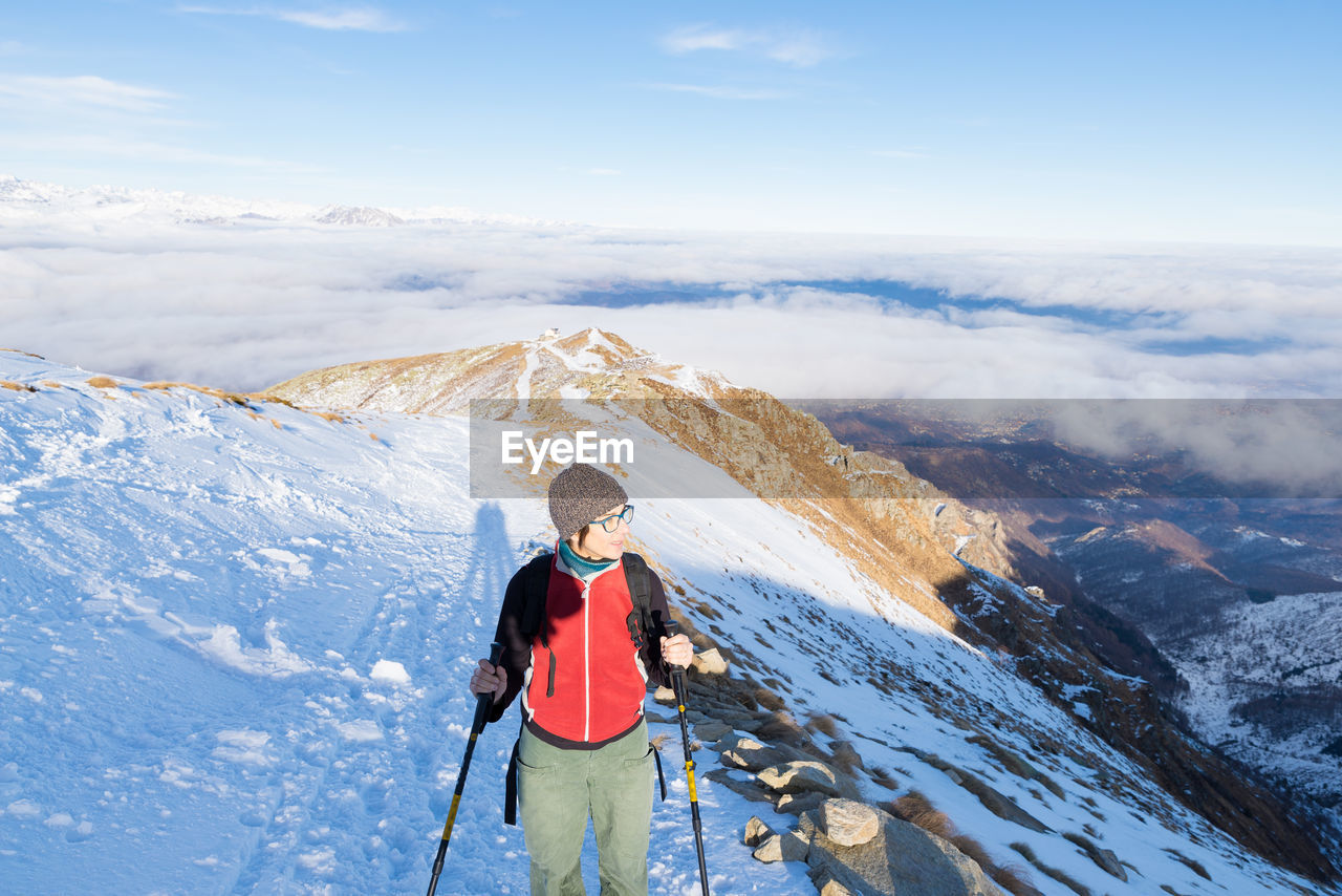 Mature woman skiing on snowcapped mountain against sky