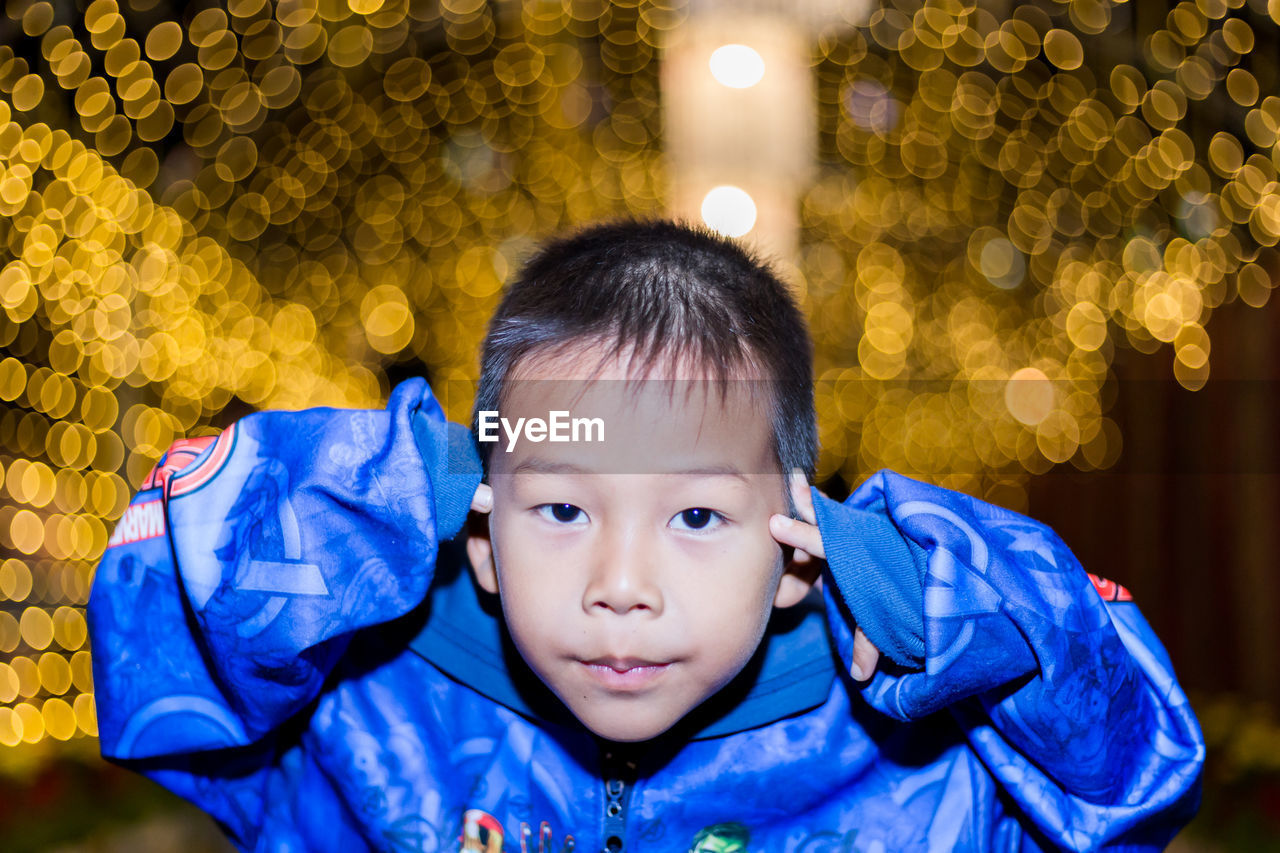 Portrait of cute boy in blue jacket against illuminated lights