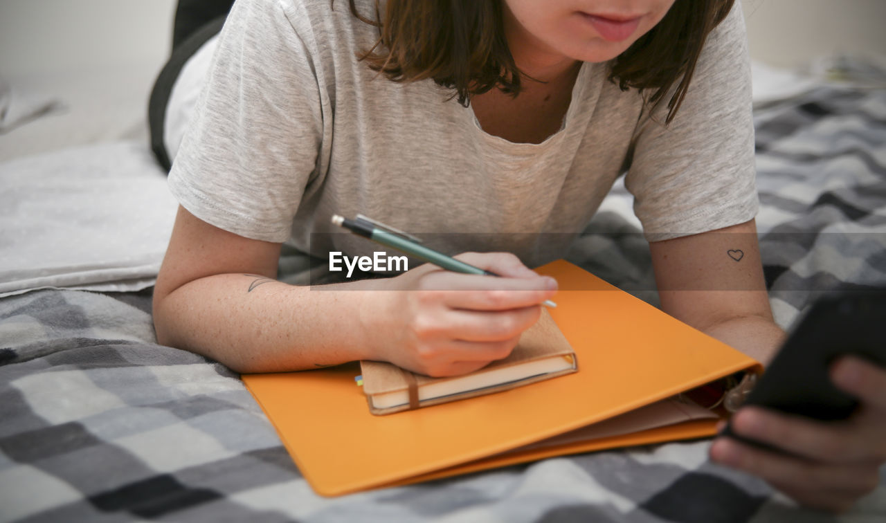 MIDSECTION OF WOMAN HOLDING BOOK WHILE SITTING BY TABLE