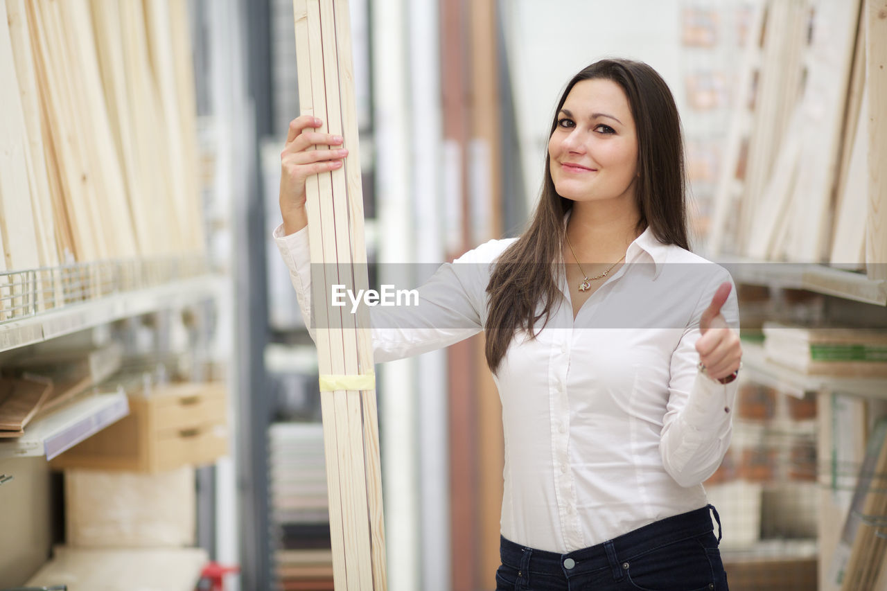 Portrait of smiling young woman showing thumbs up while holding planks in store