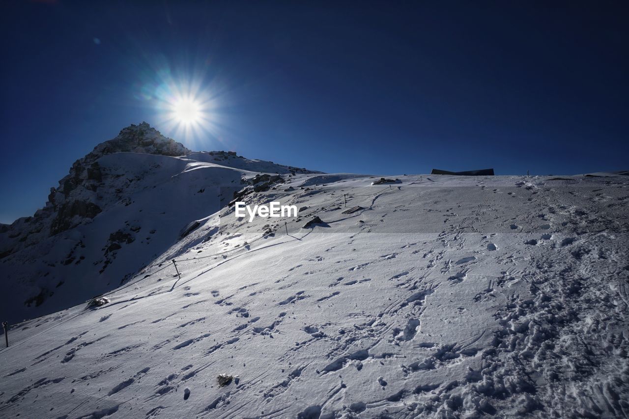 Scenic view of snow covered mountains against bright sun