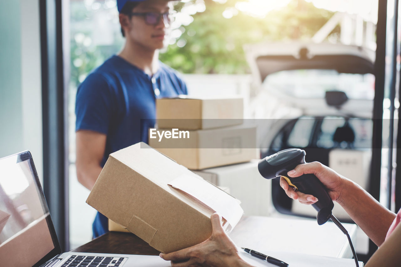 Cropped hands of woman scanning box with delivery man