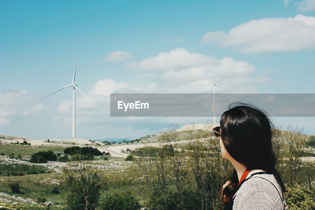 Side view of woman standing against windmills on landscape
