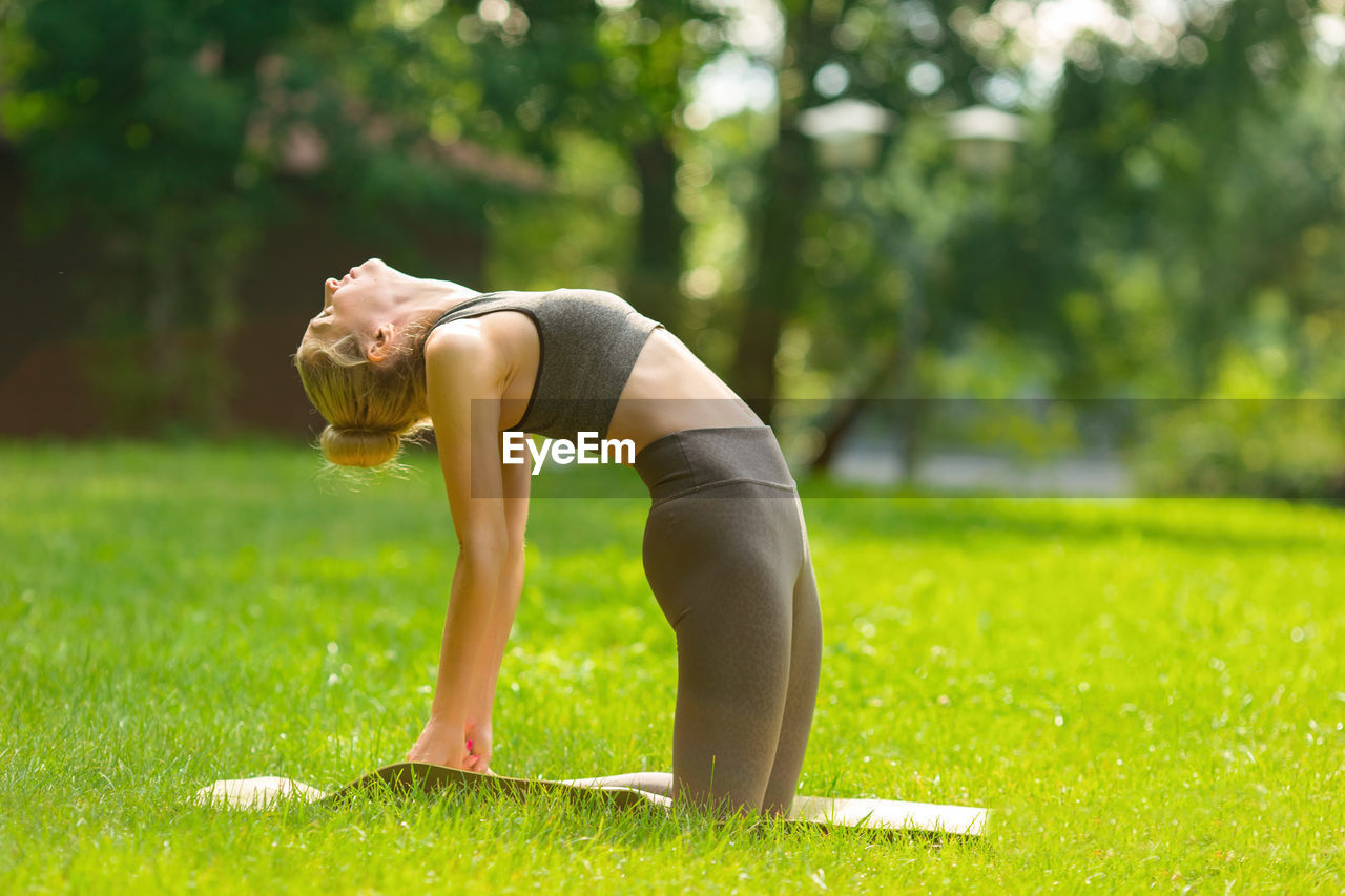 A slender woman on mat in the park, performing yoga on green mat