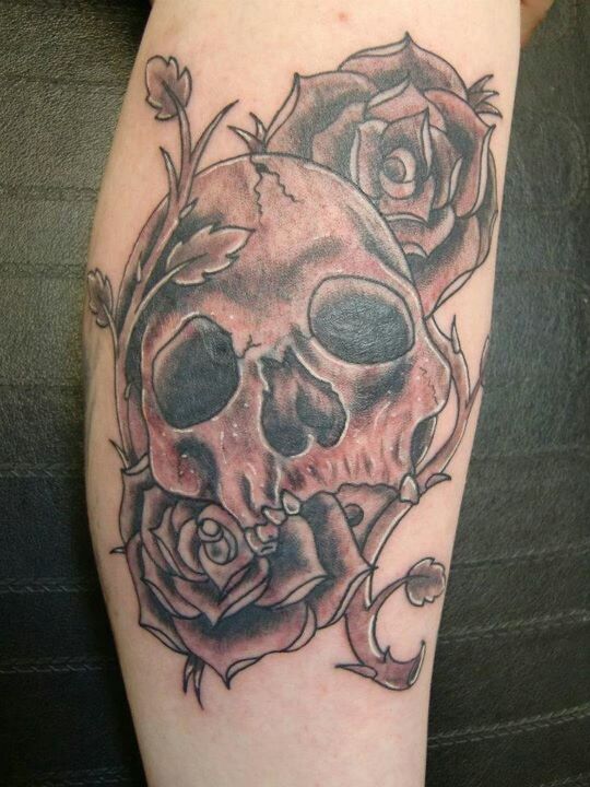 Tattoo of skull surrounded by vines and roses on hand