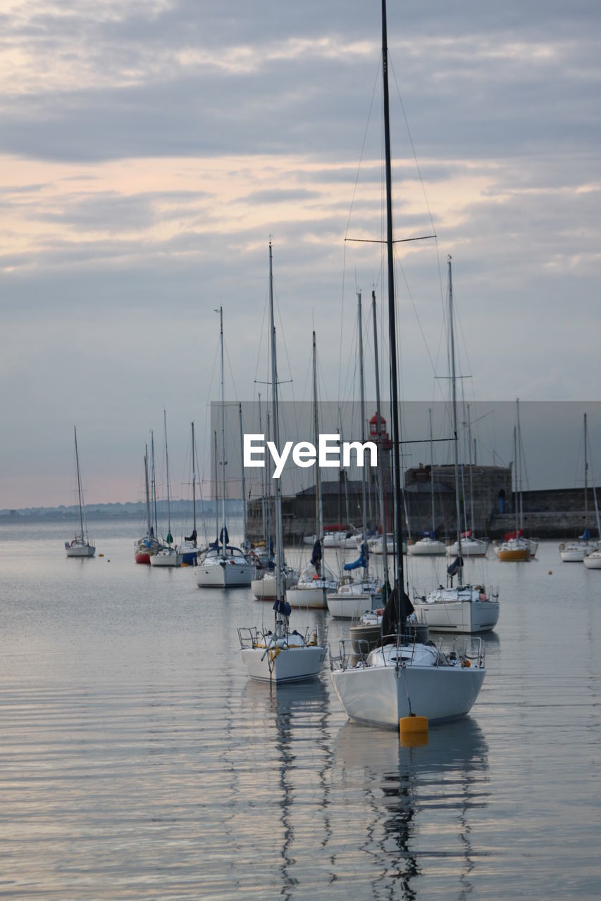 Sailboats moored on sea against sky during sunset