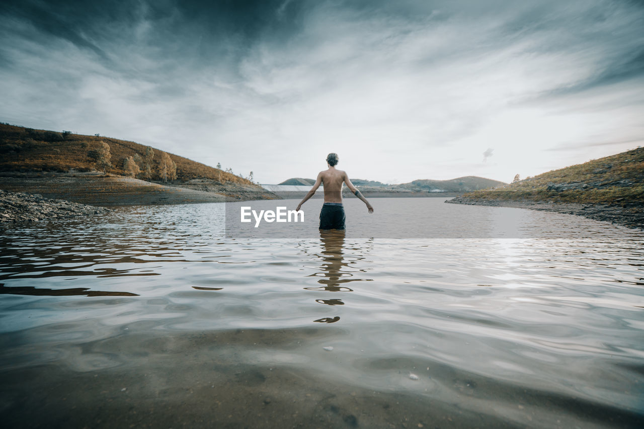 Rear view of man standing in lake against sky