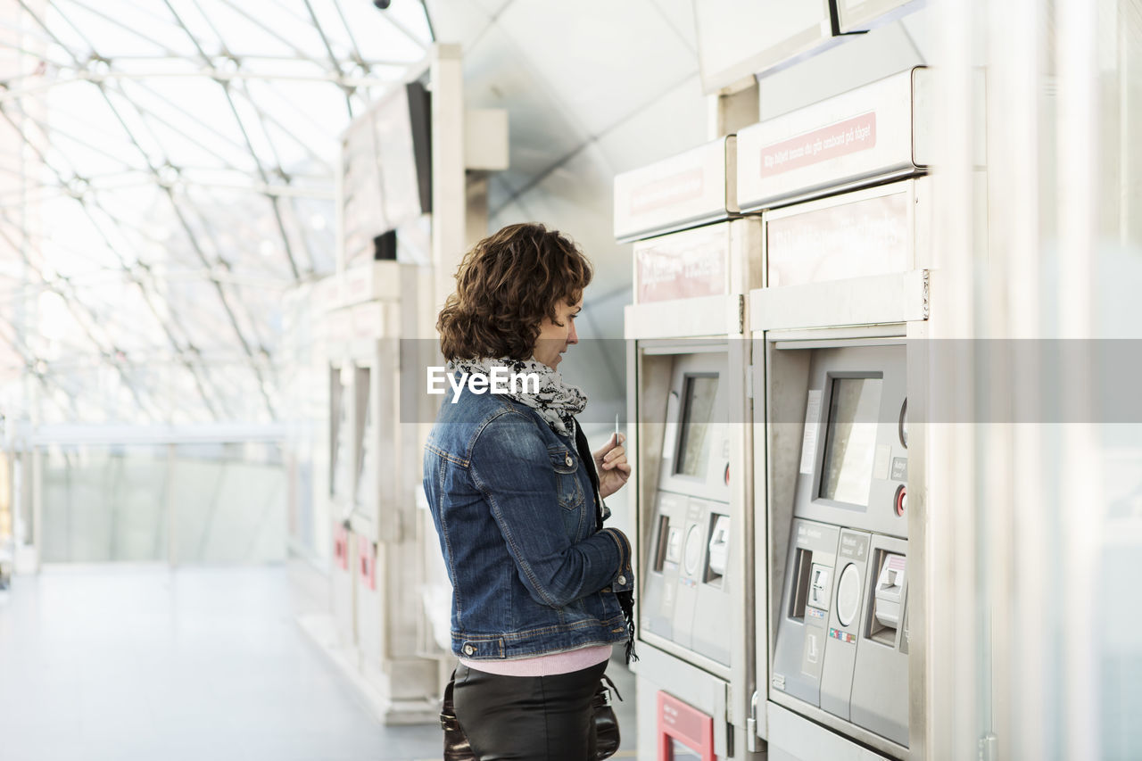 Side view of businesswoman looking at ticket machine in railway station