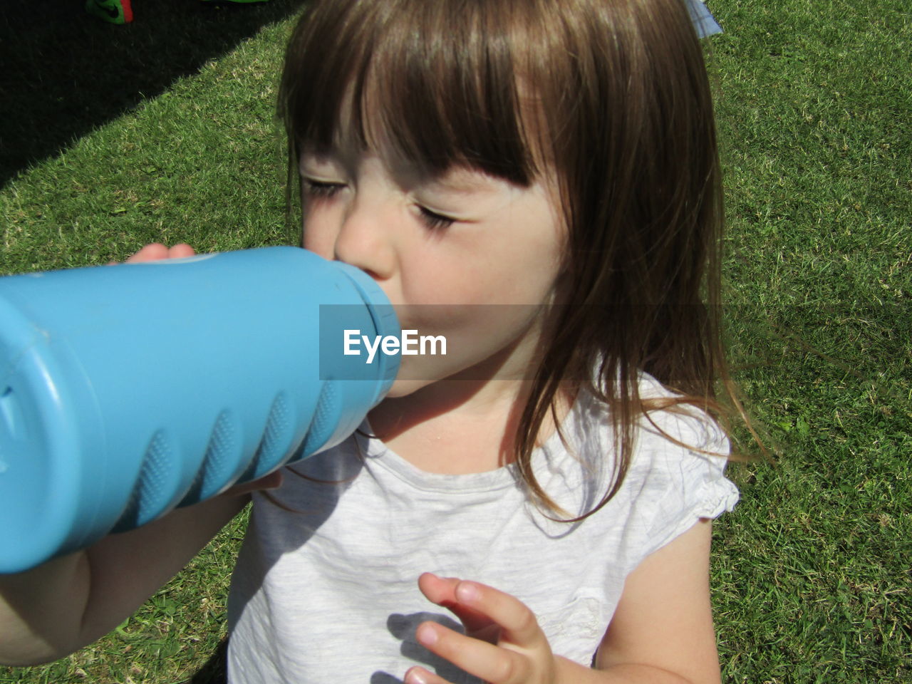 Girl with closed eyes drinking water from bottle while standing on field