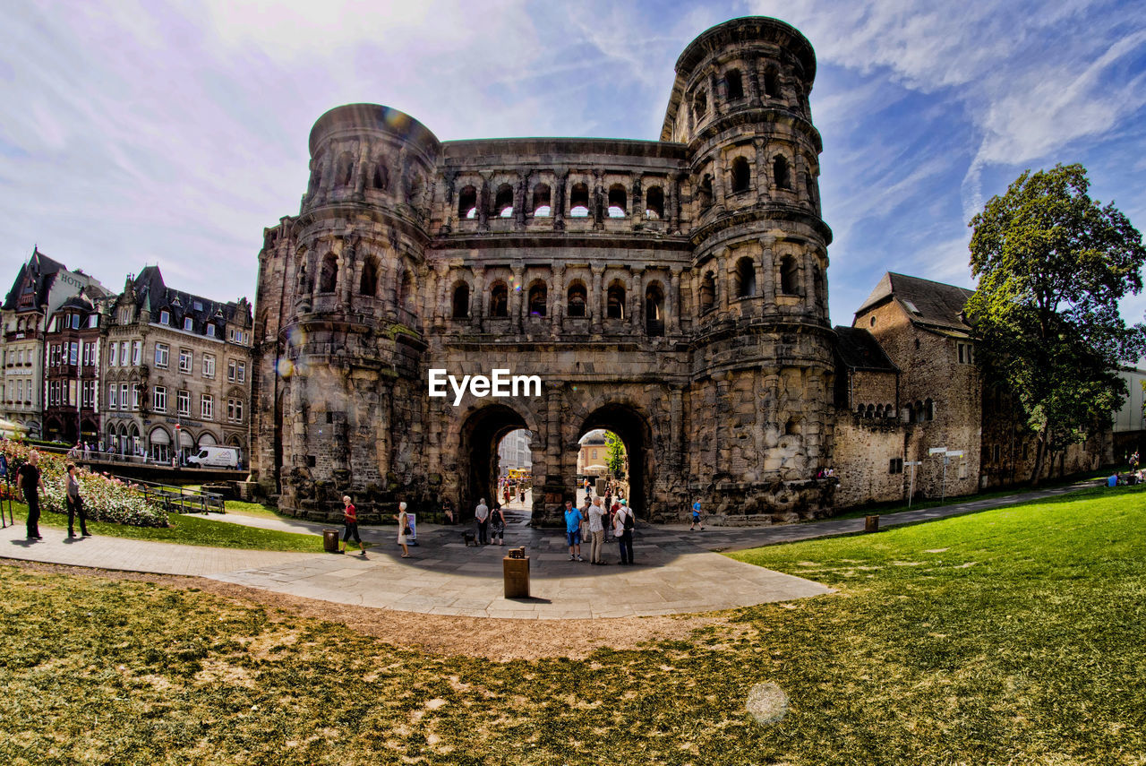 People at historic porta nigra against sky on sunny day