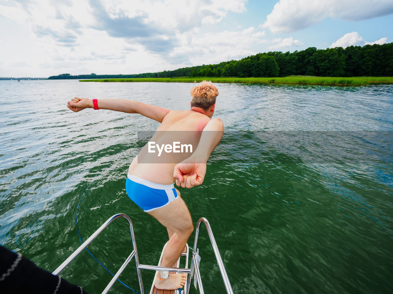 Young man jumping from a sailing yacht deck into a lake, view from back