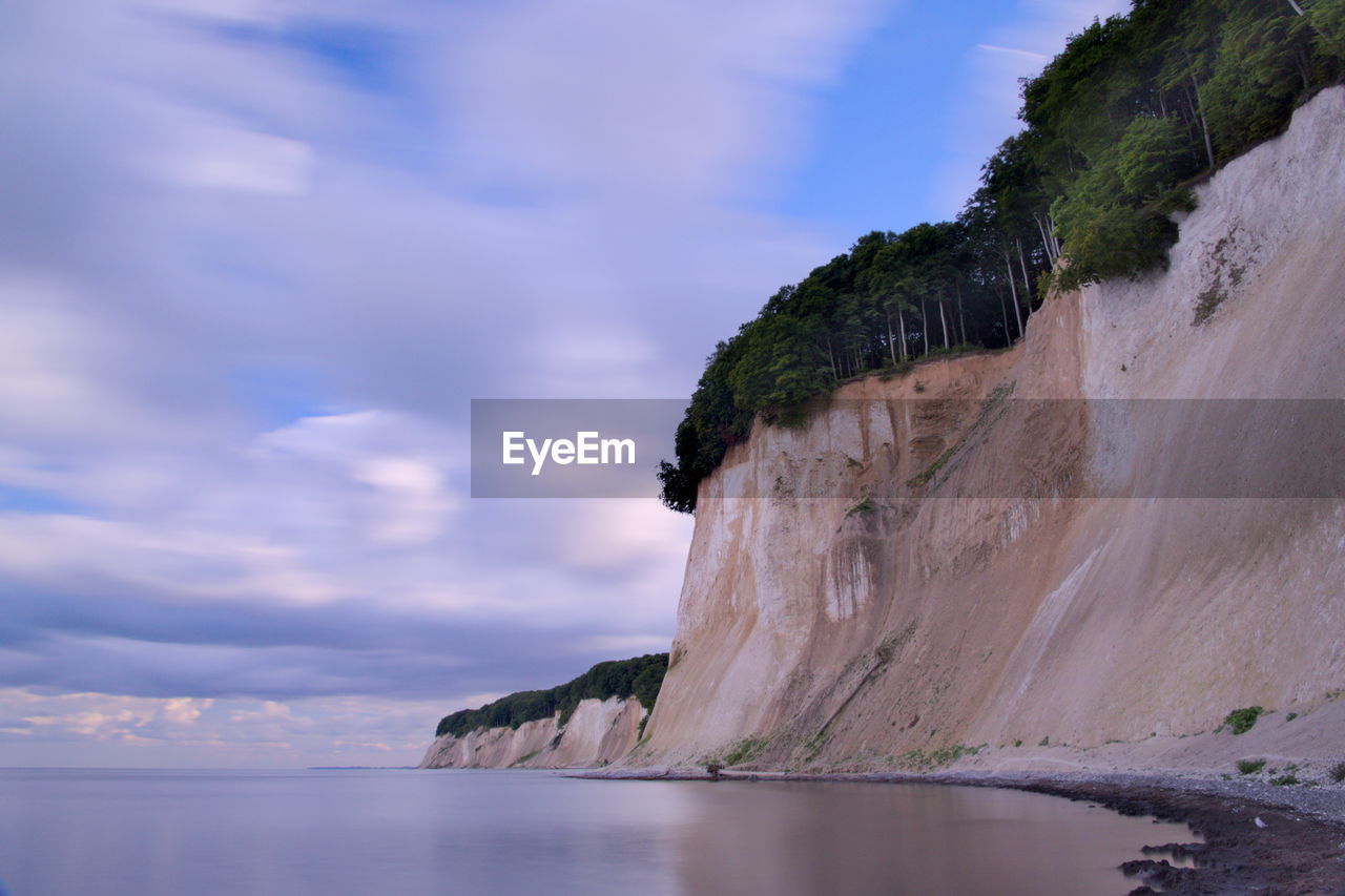 Scenic view of cliff at sea shore against sky