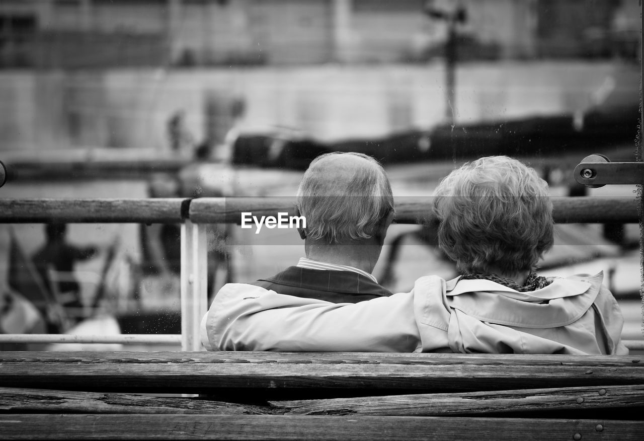 Rear view of couple sitting on bench at pier