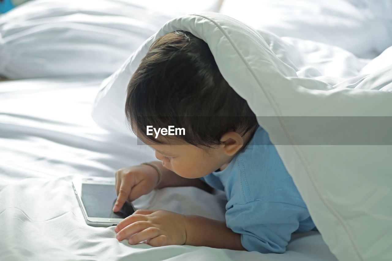 High angle view of baby boy using phone while lying on bed at home