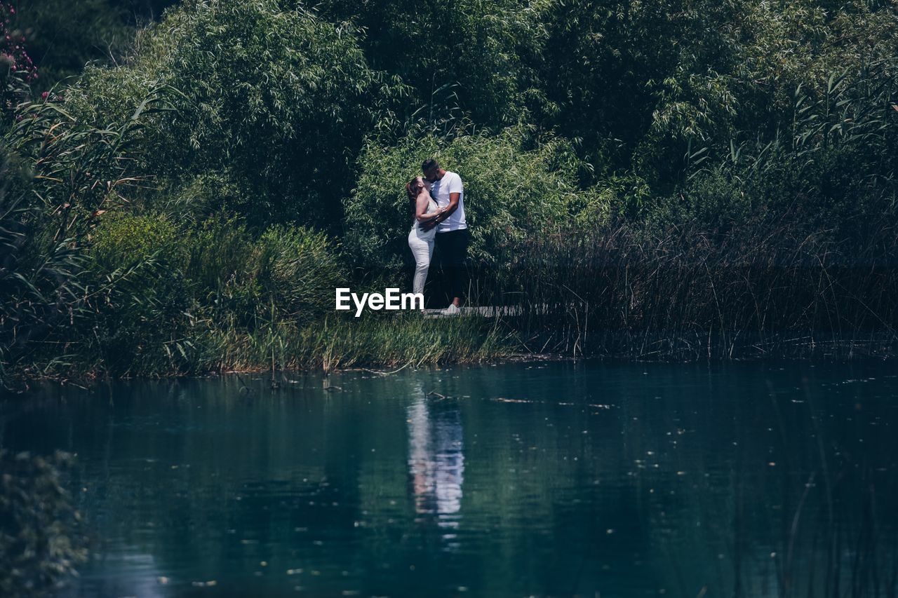 WOMAN STANDING BY LAKE AGAINST TREE