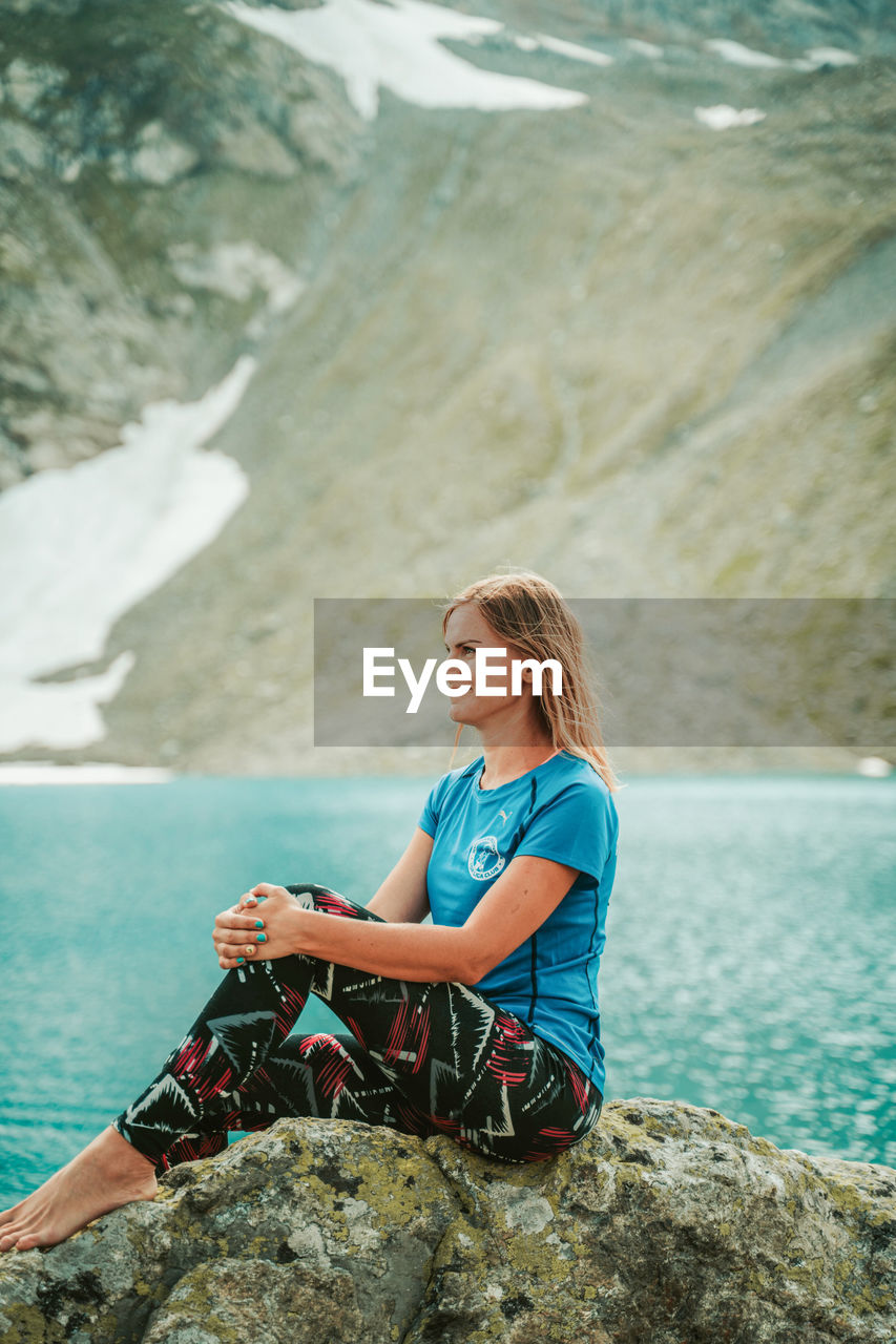 WOMAN SITTING ON ROCKS BY SEA