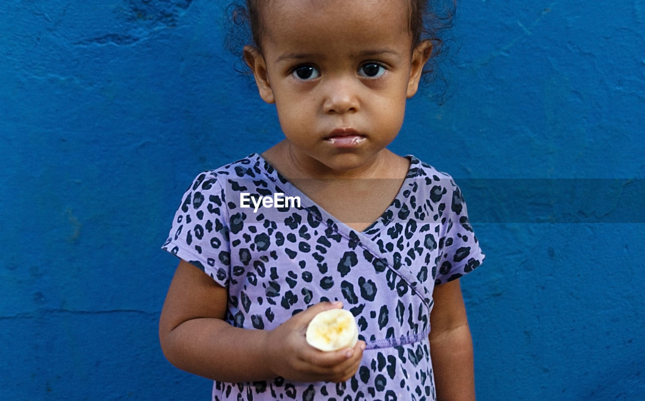 Portrait of girl holding food standing against blue wall
