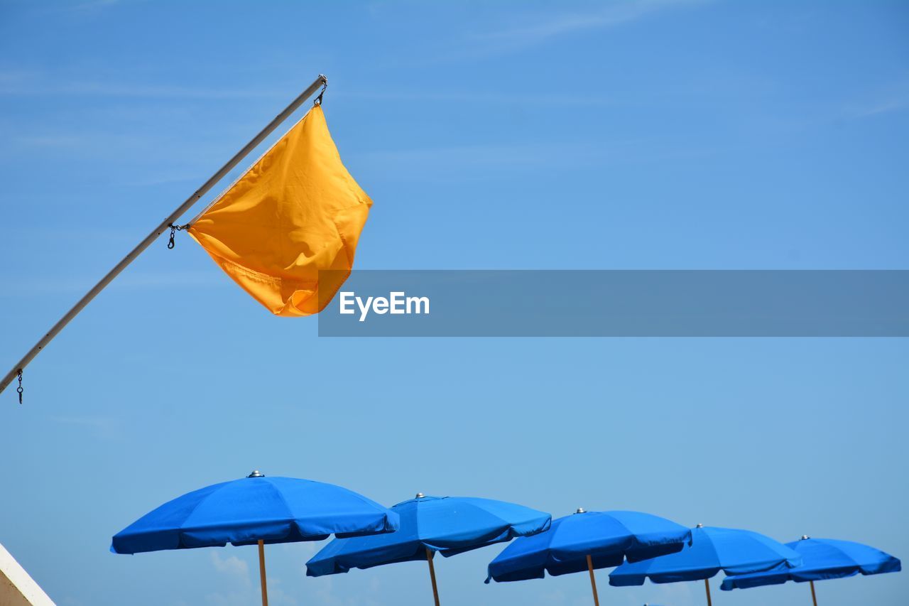 Flag and umbrellas at the seashore against blue sky