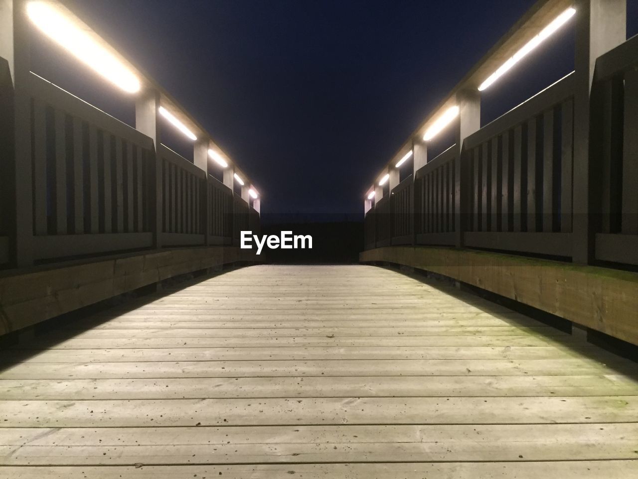 Illuminated fluorescent lights on footbridge railing at night