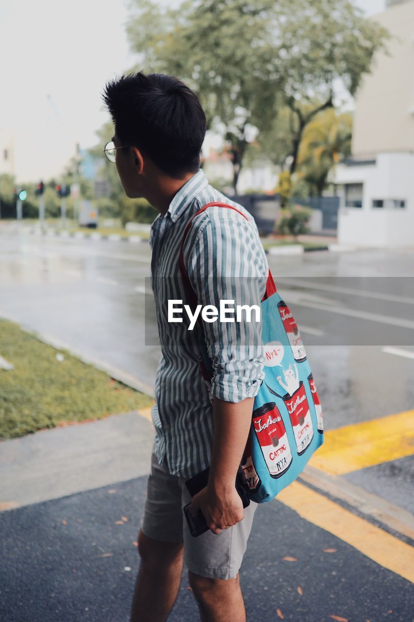 Man carrying tote bag while standing at roadside in city