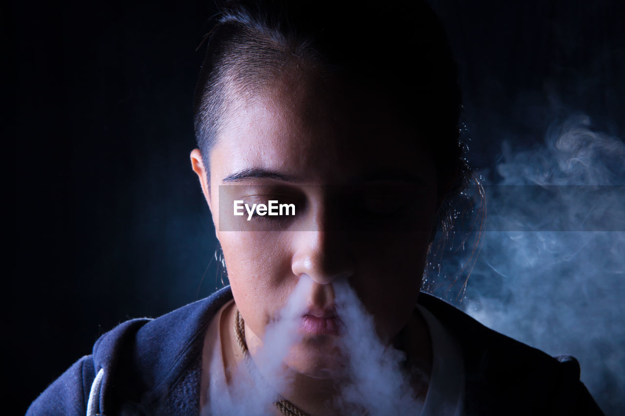Close-up of woman emitting smoke from nose against black background