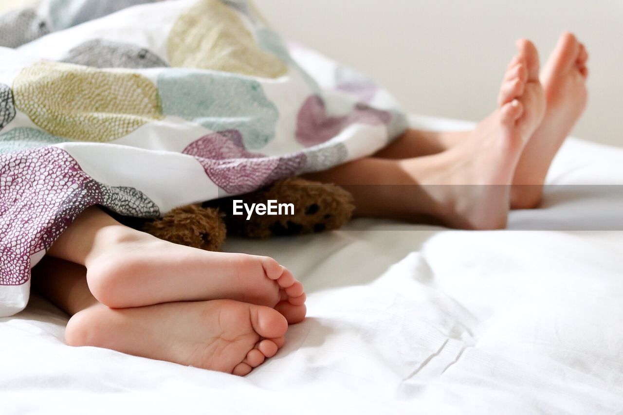 Low section of children resting with teddy bear on bed