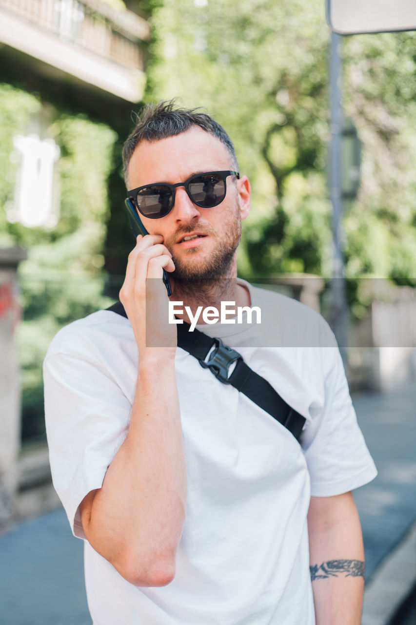 YOUNG MAN USING MOBILE PHONE WHILE STANDING ON CAMERA