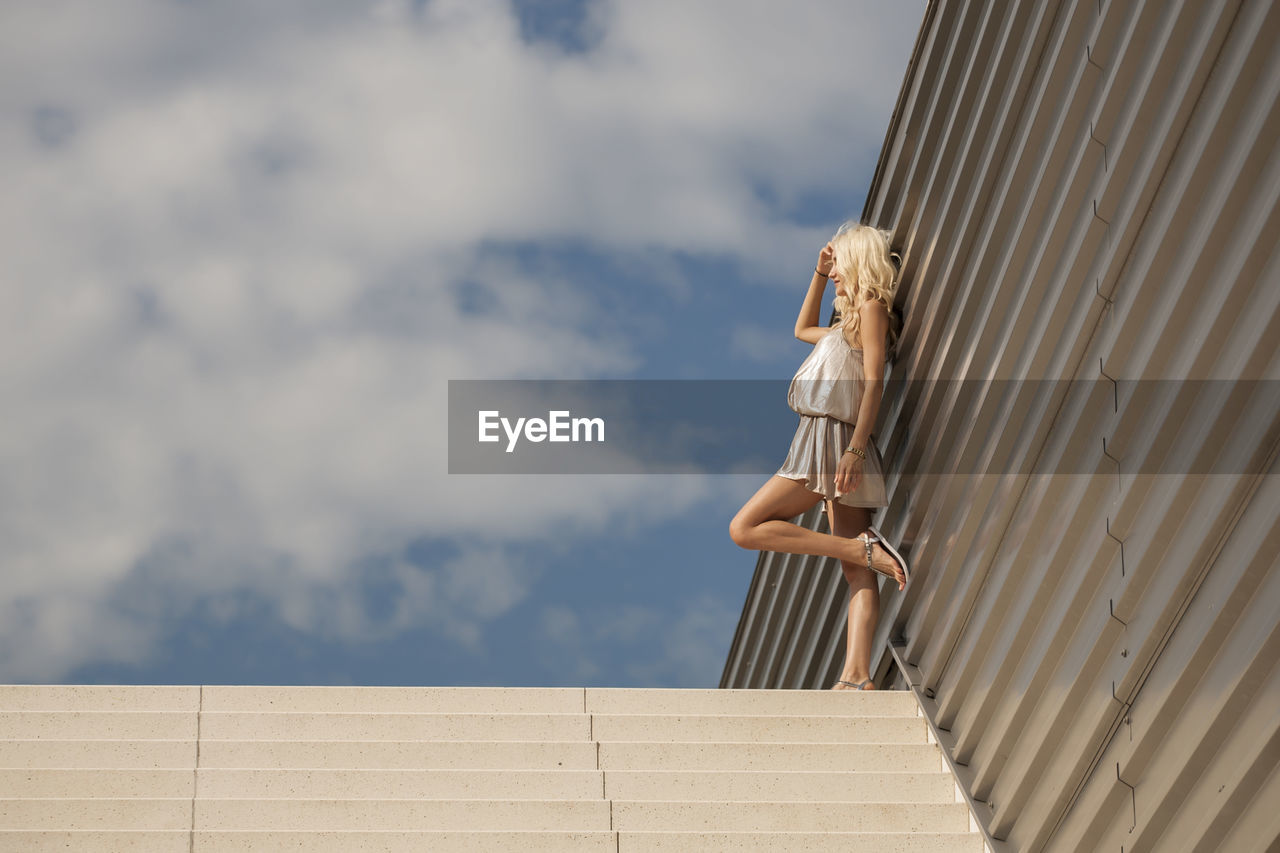 Low angle view of woman standing on steps against sky