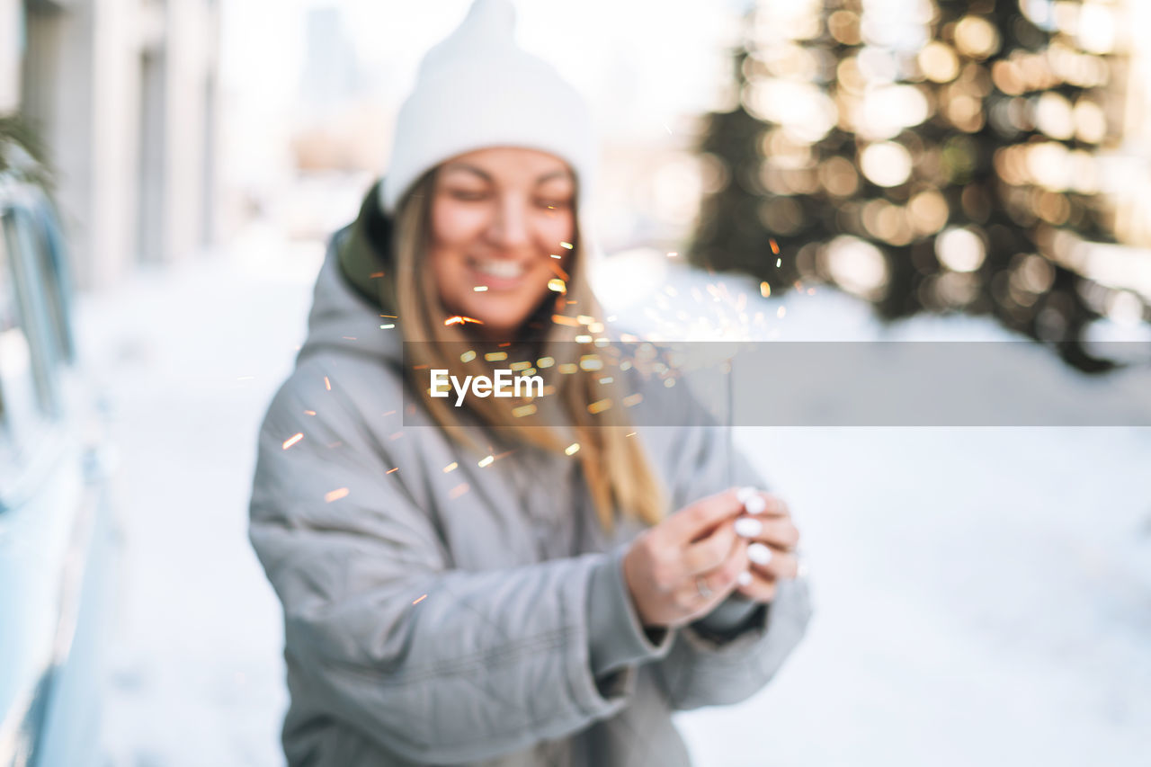 Blurred motion photo of young woman in warm clothes with sparkler near retro car in winter street