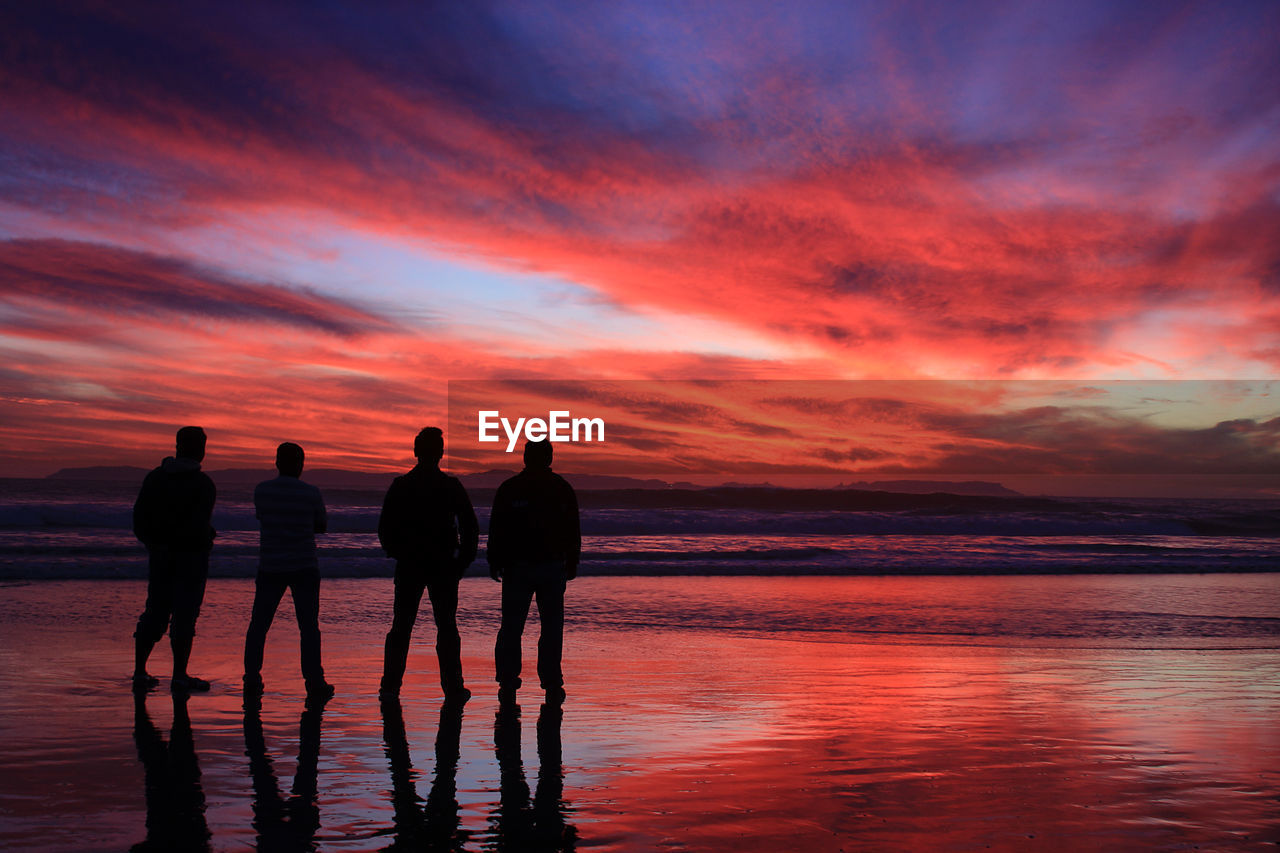 Silhouette of four people standing in sea at sunset
