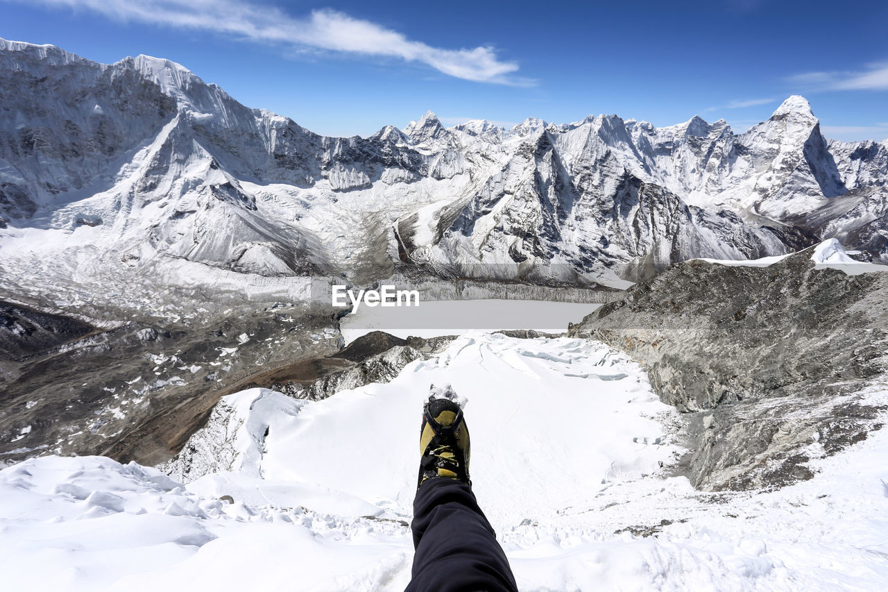 Low section of person on snowcapped mountains against sky
