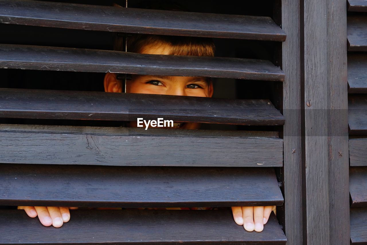 Portrait of boy seen through wooden window