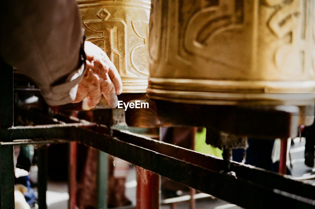 Cropped hand of man touching prayer wheels in temple