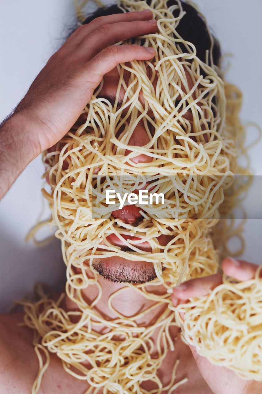 Close-up of young man covered in spaghetti against wall